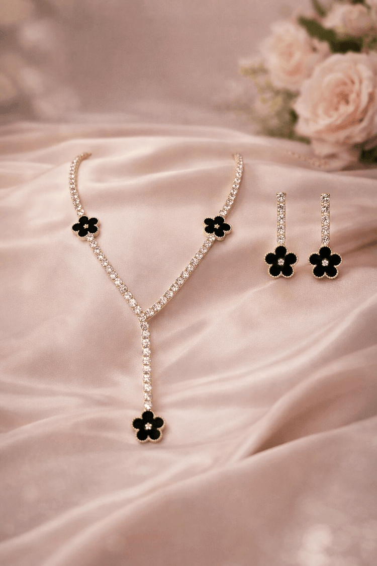 Necklace and earrings with black flower details on a pink fabric background