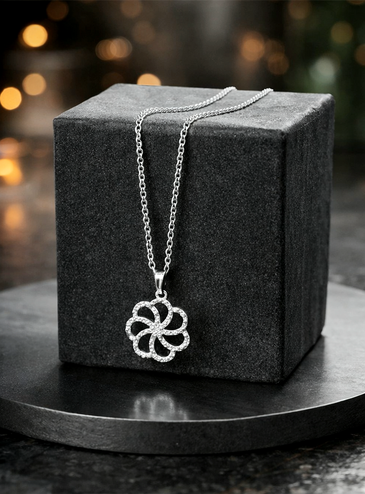 Silver necklace with a floral pendant on a dark gray cube against a blurred background