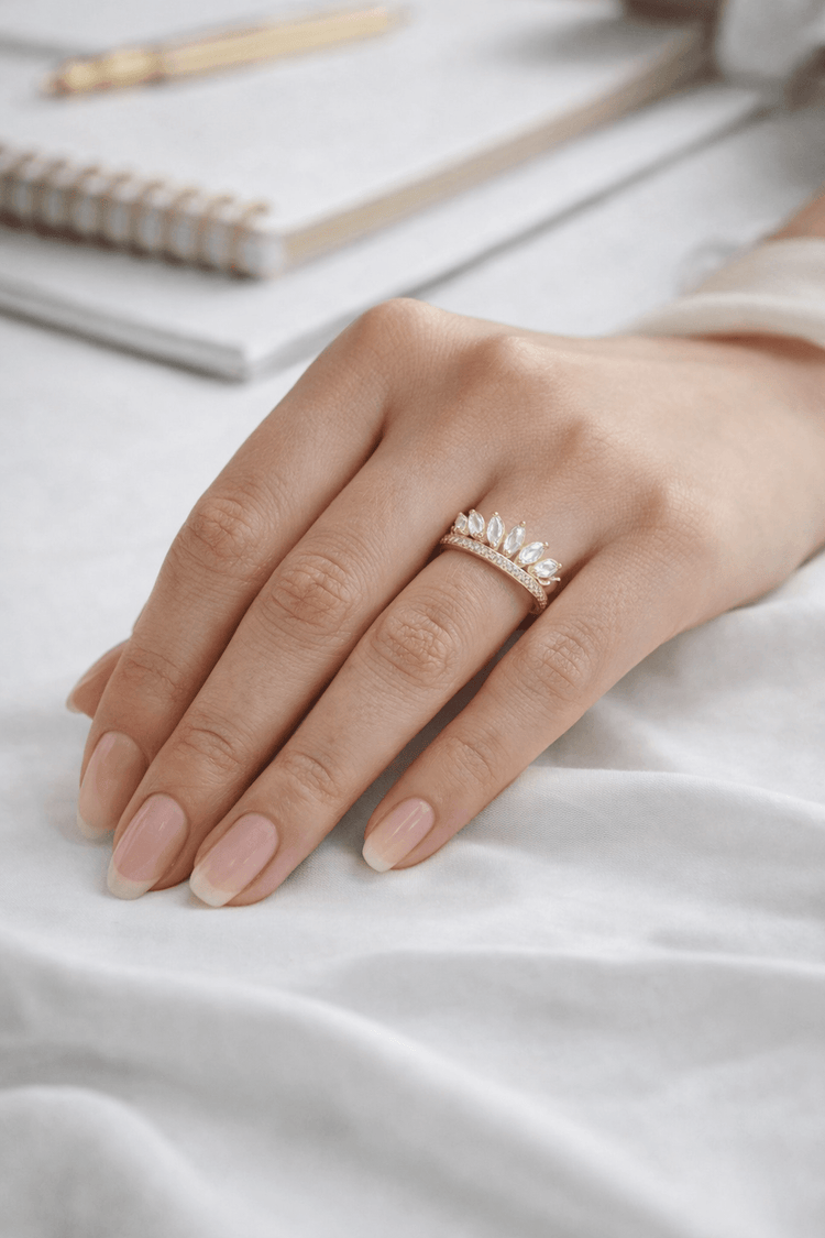 Hand wearing a gold ring on a white surface with a notebook in the background
