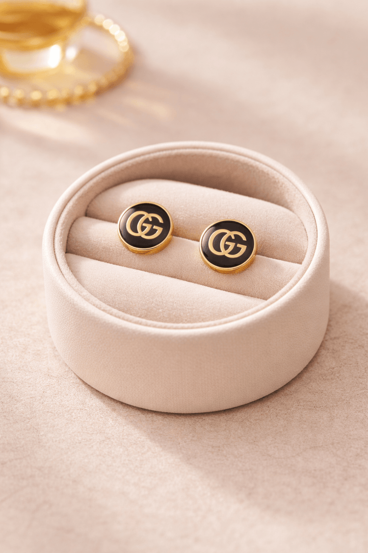 Pair of black and gold earrings in a pink jewelry box on a light pink surface.
