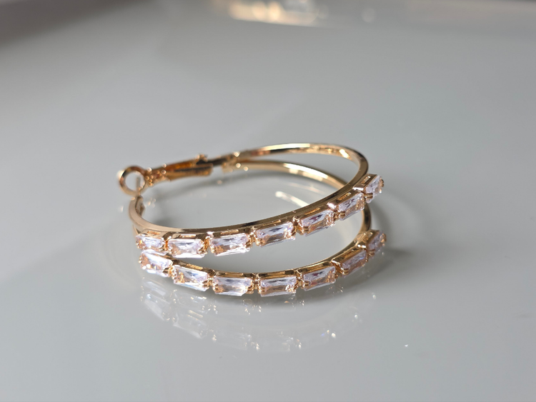 Gold hoop earrings with clear gemstones on a light gray background