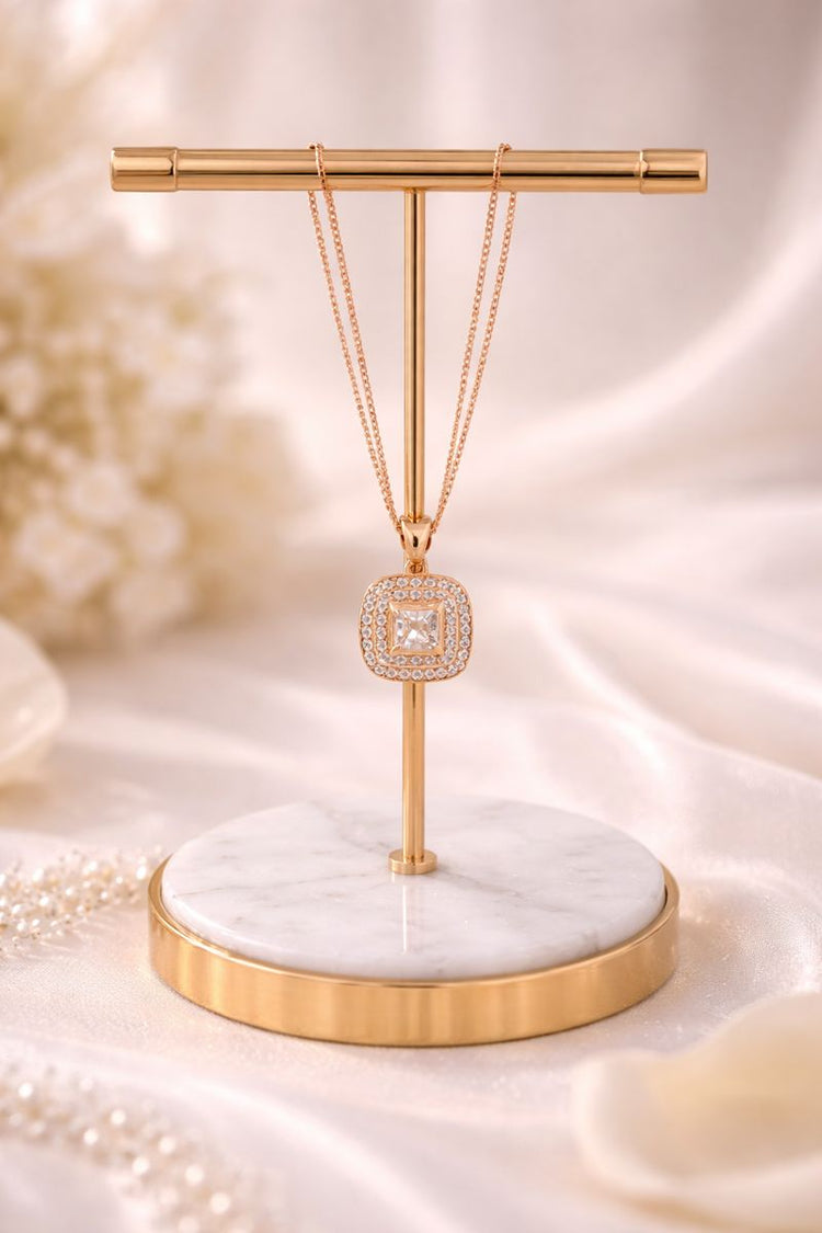 Necklace with a diamond pendant on a gold and marble stand against a soft, blurred background.