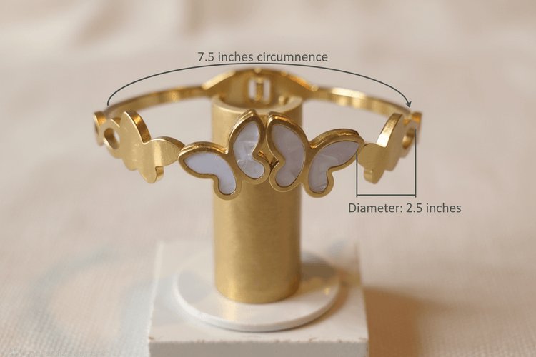 Gold bracelet with butterfly designs on a cylindrical stand against a beige background
