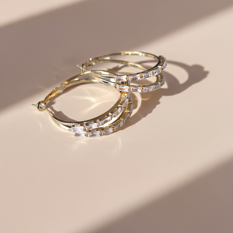 Gold hoop earrings with clear stones on a beige surface