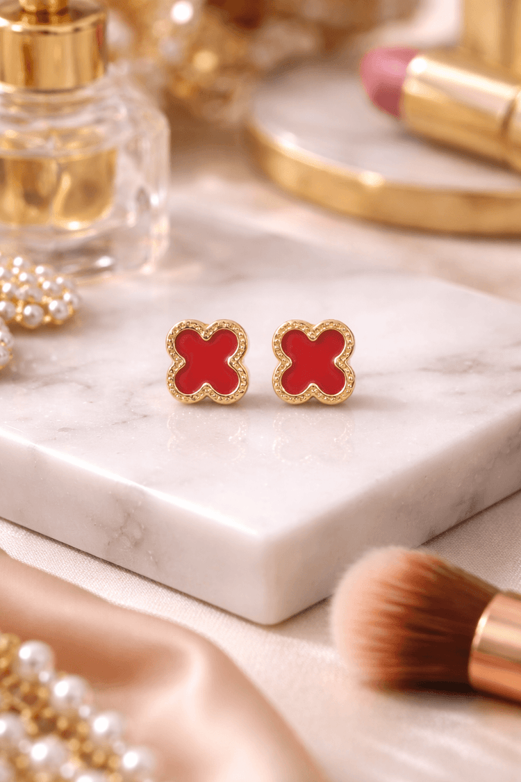 Red and gold butterfly-shaped earrings on a marble surface with makeup items.