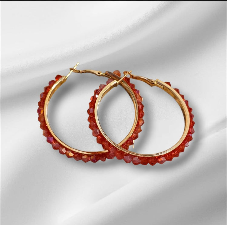 Gold hoop earrings with red gemstones on a white fabric background