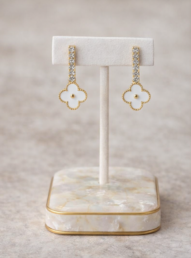 Pair of gold and white floral earrings on a marble stand with a beige background