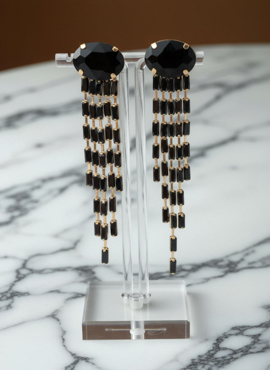 Black beaded earrings on a clear stand against a marble background
