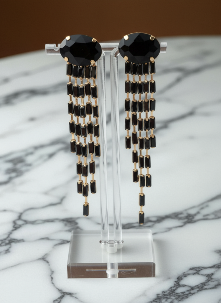 Black beaded earrings on a clear stand against a marble background