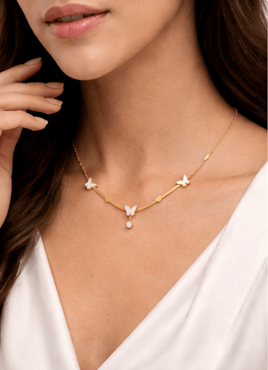 Gold necklace with butterfly pendants worn by a person in a white top.