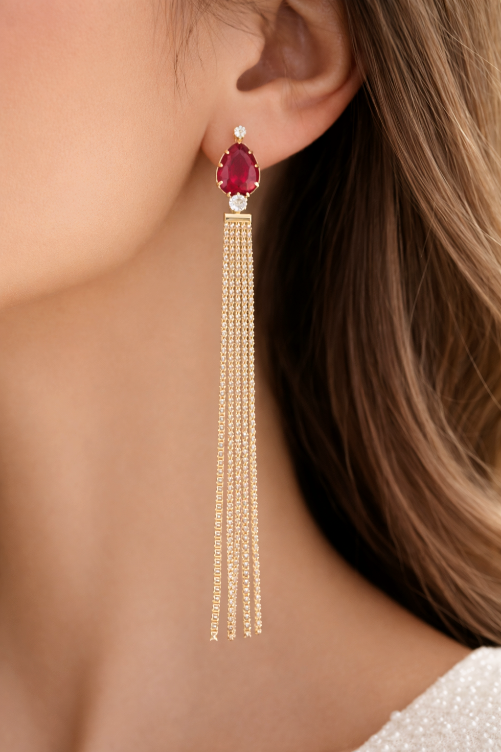 Gold earrings with a red gemstone worn by a person