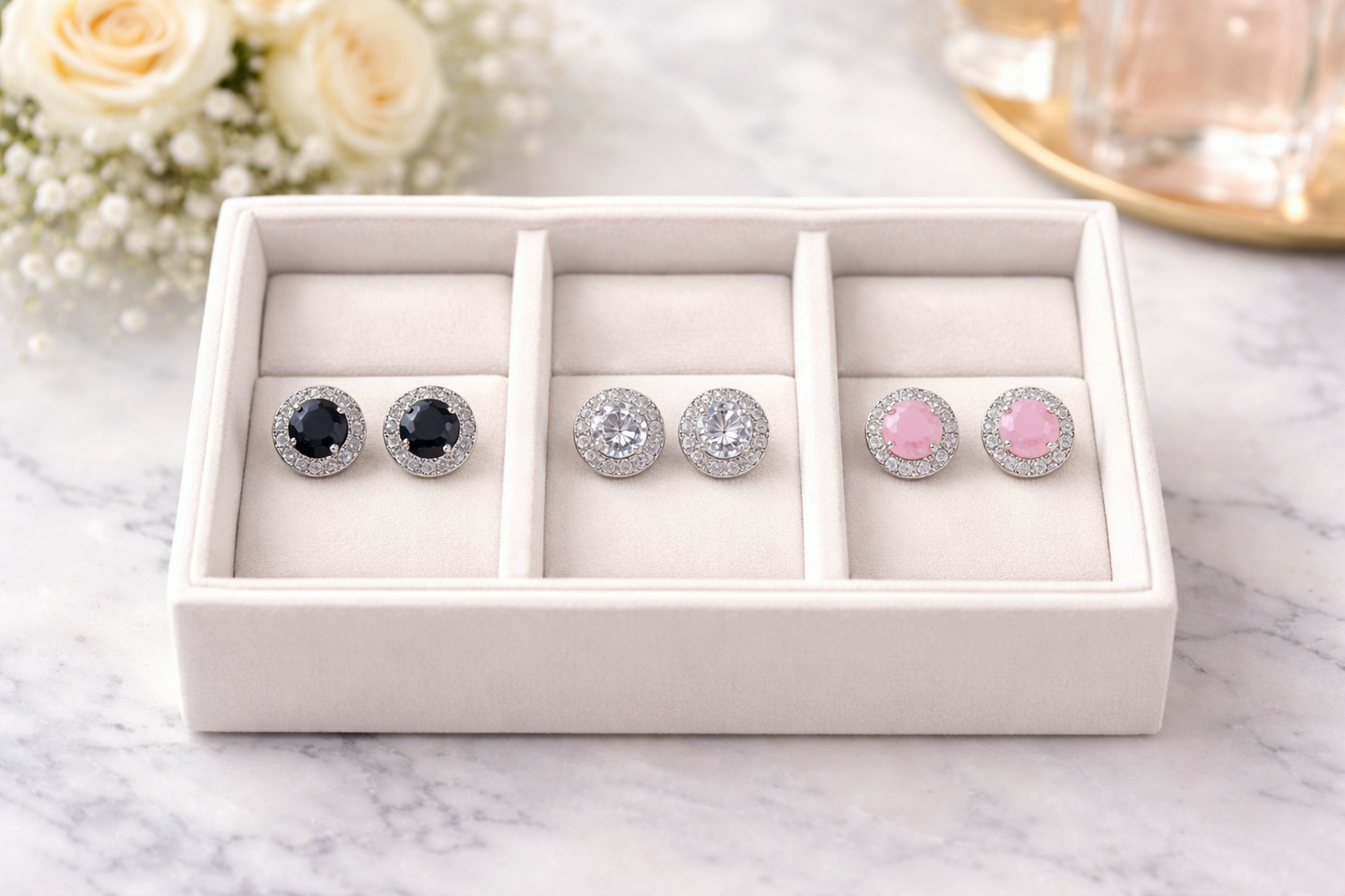 Set of earrings in a white jewelry box on a marble surface with flowers in the background