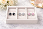 Set of earrings in a white jewelry box on a marble surface with flowers in the background