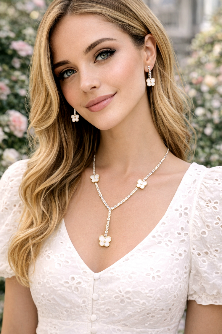 Woman wearing a white lace top and floral jewelry with a blurred floral background