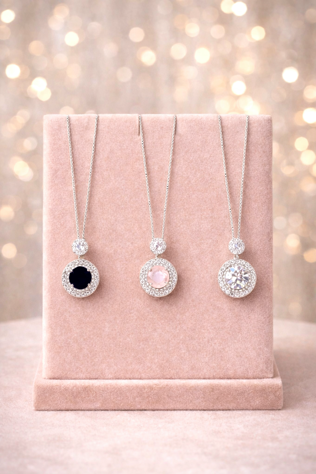 Three necklaces with round pendants on a pink velvet stand against a blurred light background