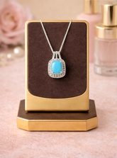 Turquoise pendant necklace on a gold and brown display stand with a soft pink background.