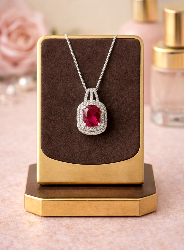 Jewelry display with a necklace featuring a red gemstone on a brown card.