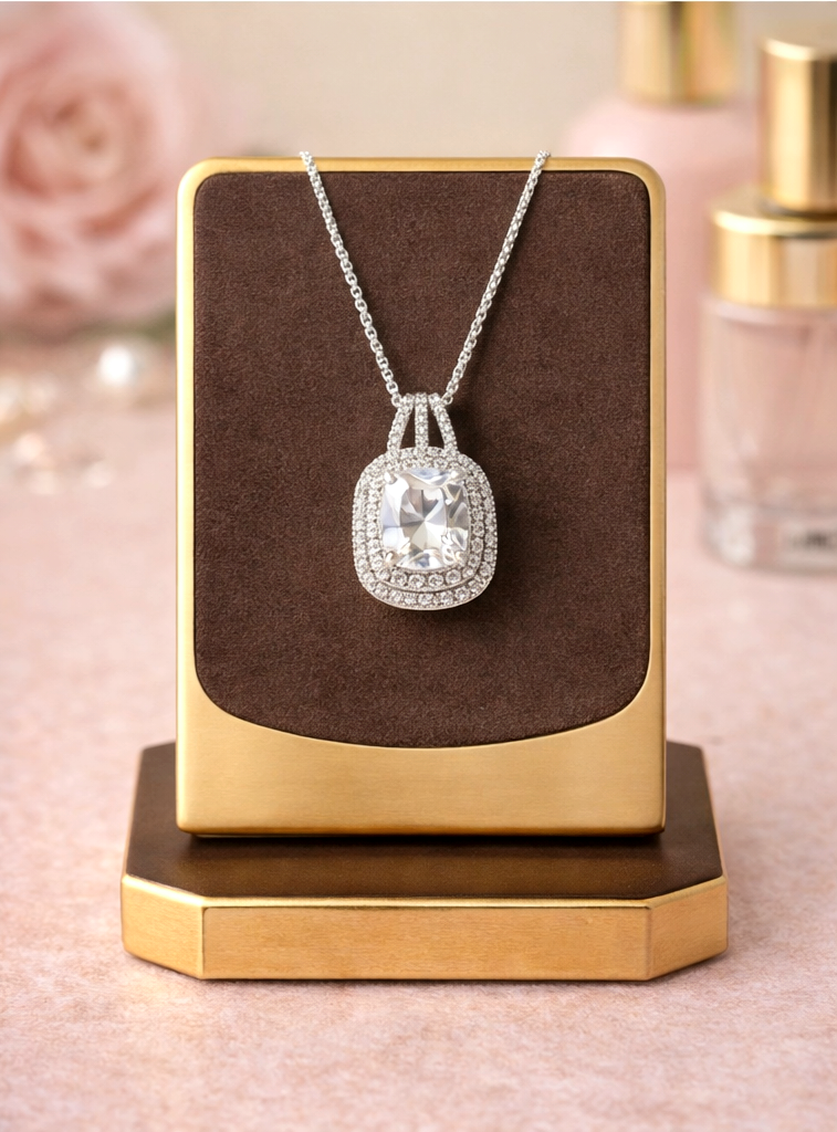 Silver necklace with a large diamond pendant on a brown cushion against a pink background