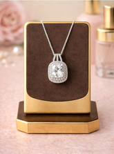 Silver necklace with a large diamond pendant on a brown cushion against a pink background