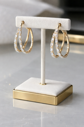 Gold hoop earrings on a white and gold display stand against a neutral background