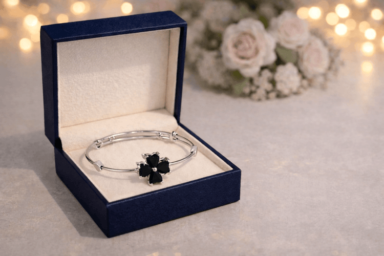 Silver bracelet with black flowers in an open blue jewelry box on a light background.