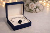 Silver bracelet with black flowers in an open blue jewelry box on a light background.