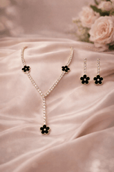 Necklace and earrings with black flower details on a pink fabric background