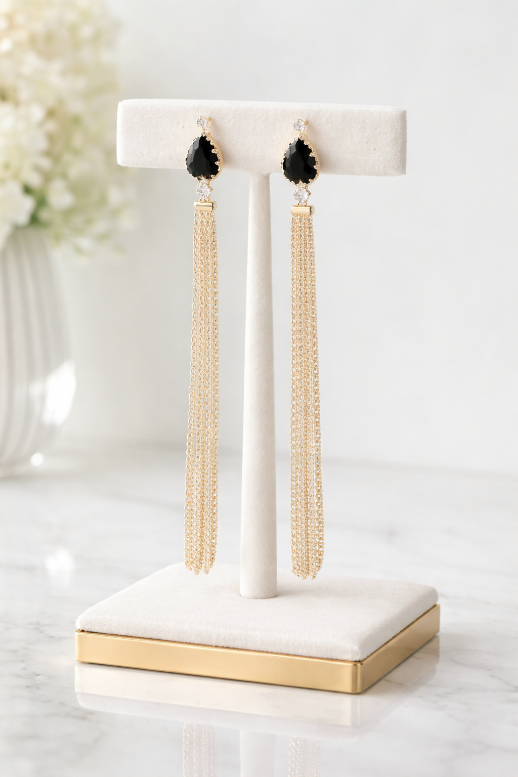 Gold tassel earrings on a white and gold stand with a blurred floral background