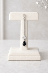 Earring with a black teardrop pendant on a white stand against a light background