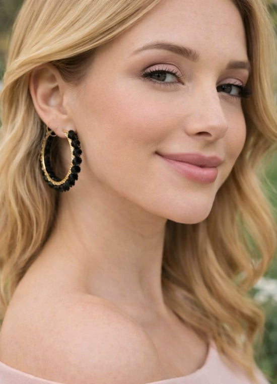 Close-up of a woman wearing gold hoop earrings with black beads.