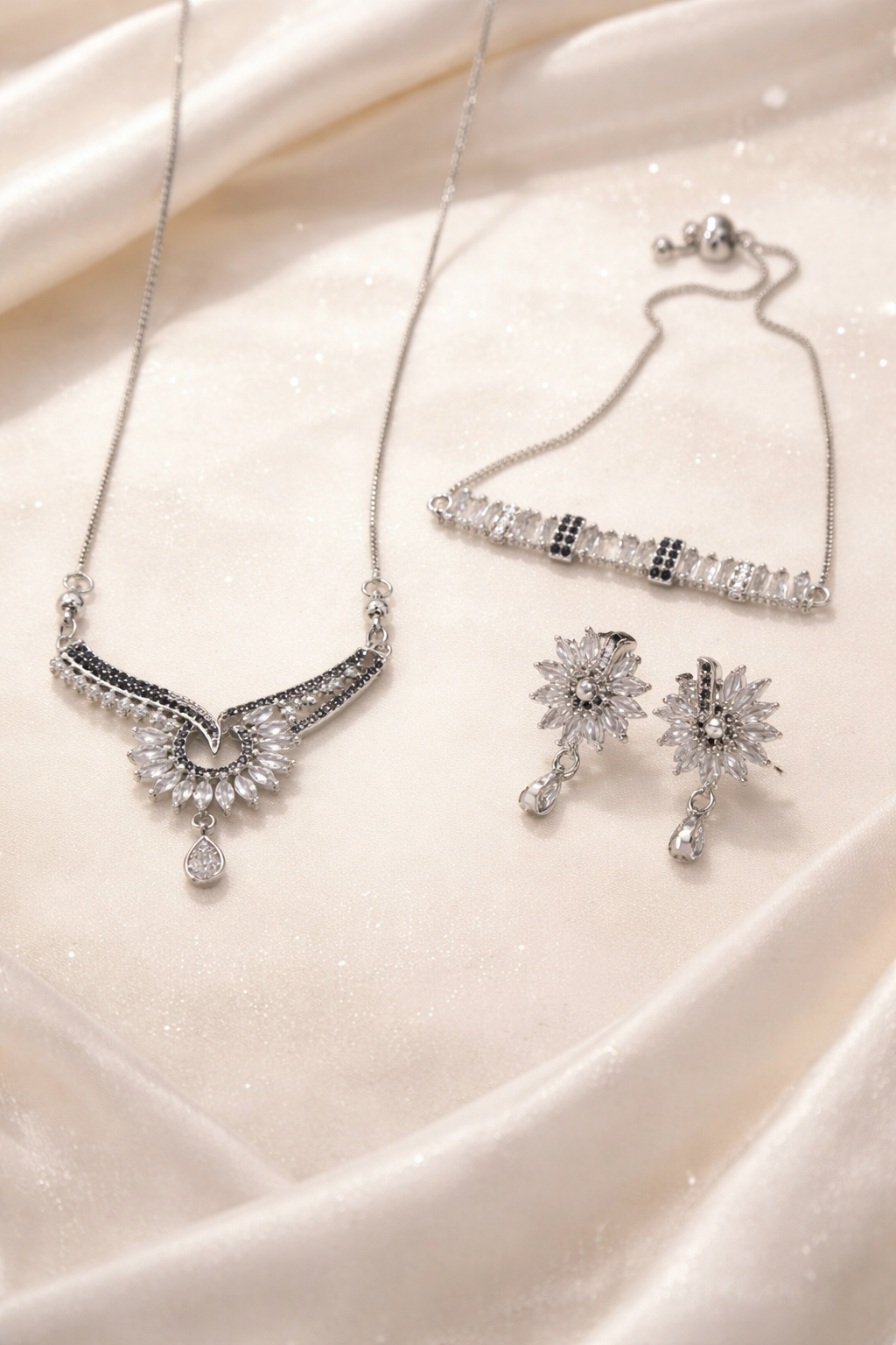 Silver necklace, bracelet, and earrings on a satin surface