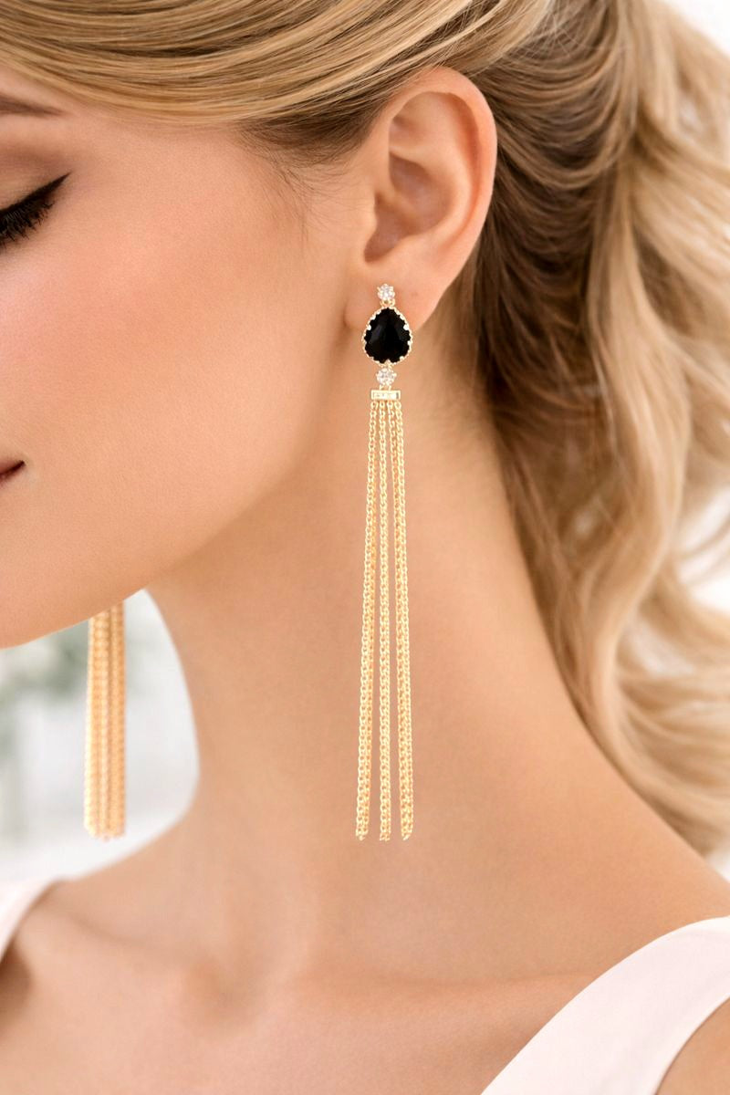 Close-up of a woman wearing gold tassel earrings with a black gemstone.