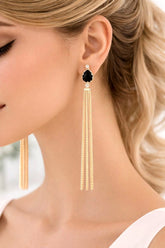 Close-up of a woman wearing gold tassel earrings with a black gemstone.