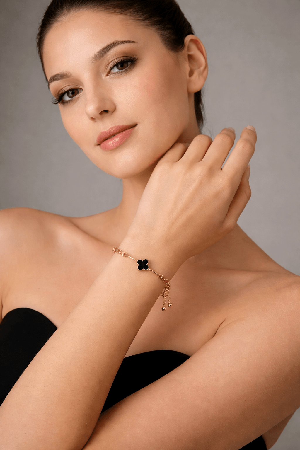 Woman wearing a gold bracelet with a black stone on a neutral background