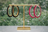 Gold earring stand with black and red hoop earrings against a blurred green background
