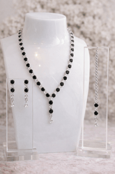Black beaded necklace and earrings on a mannequin bust with a blurred background