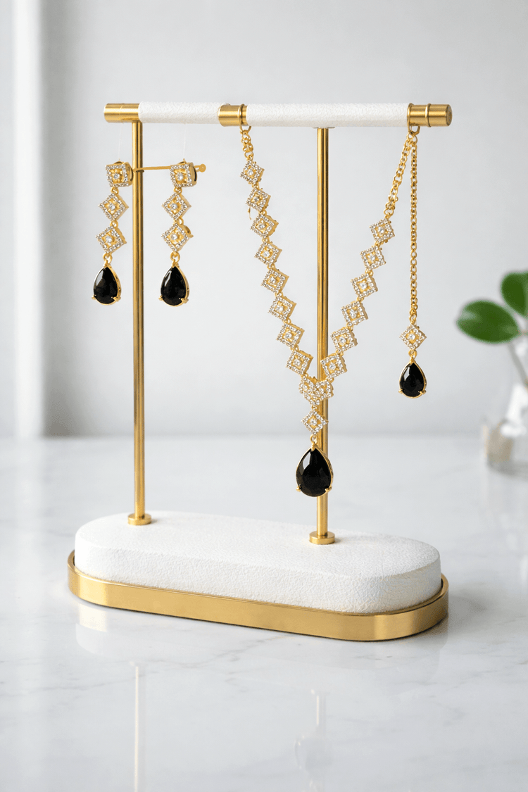 Gold and black earrings on a white and gold stand against a light background