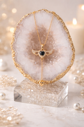 Gold necklace with a black heart pendant on a crystal stand with blurred lights in the background
