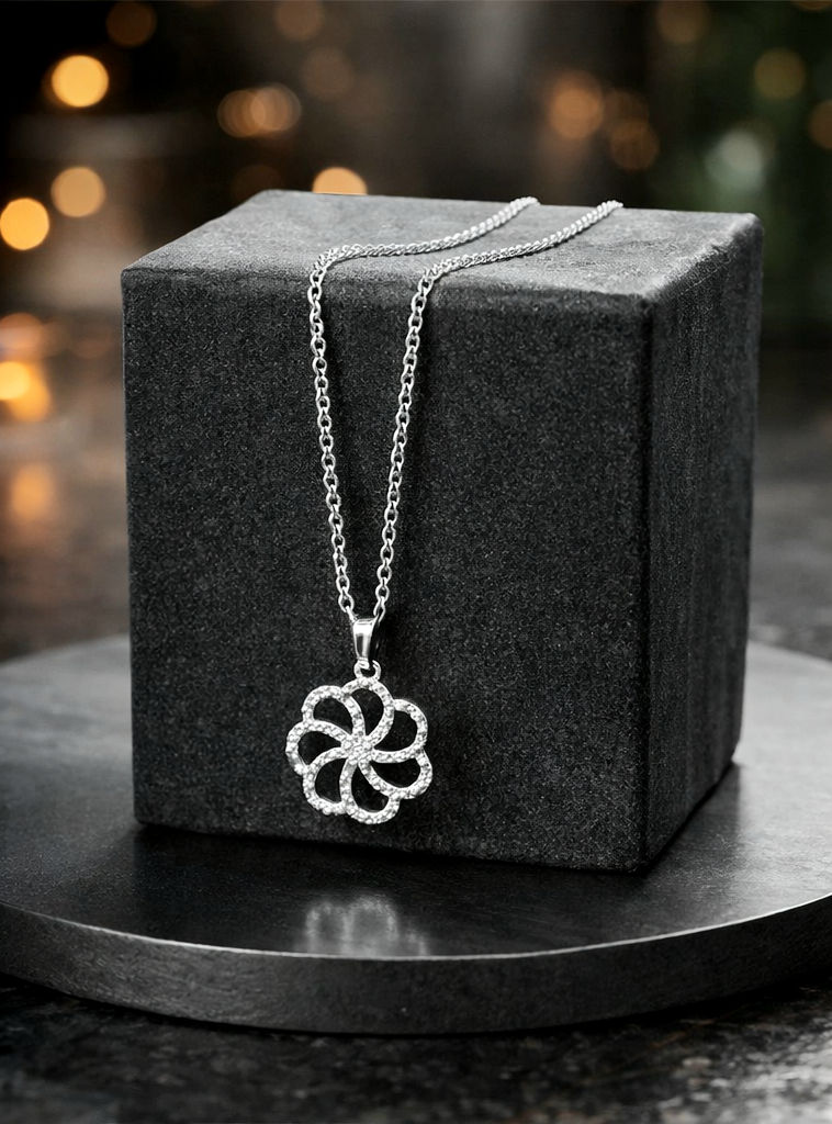 Silver necklace with a floral pendant on a dark gray cube against a blurred background