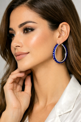 Woman wearing a blue hoop earring against a neutral background
