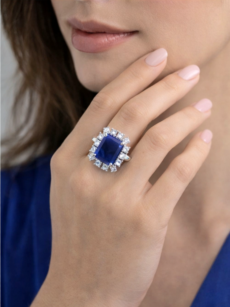 Close-up of a hand wearing a ring with a blue gemstone and diamond accents.