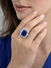 Close-up of a hand wearing a ring with a blue gemstone and diamond accents.
