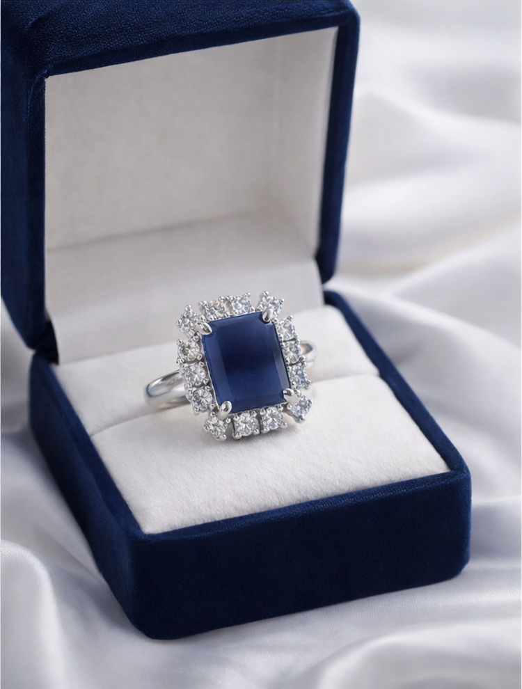 Blue gemstone ring in a blue velvet box on a white fabric background