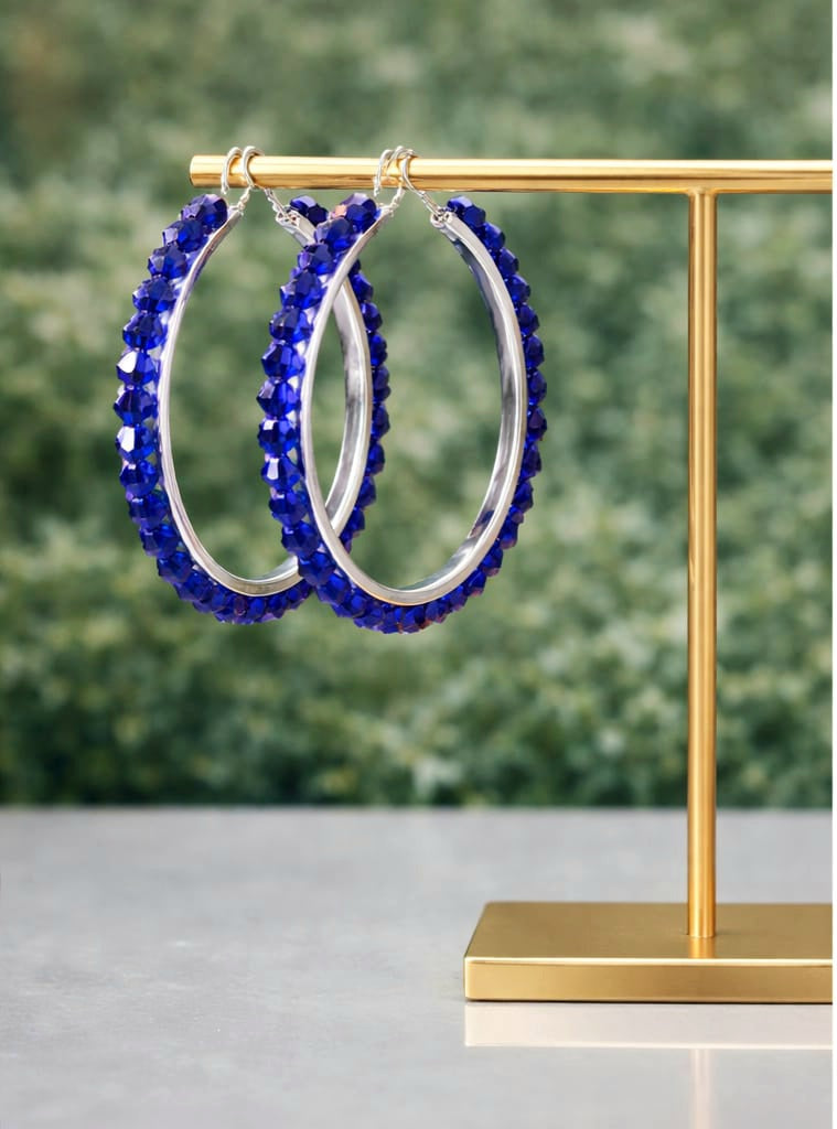 Blue beaded hoop earrings on a gold stand with a blurred green background