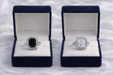 Two diamond rings in open blue velvet boxes on a white fabric background