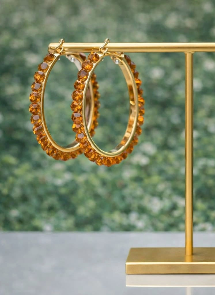 Gold hoop earrings with orange gemstones on a gold stand against a blurred green background
