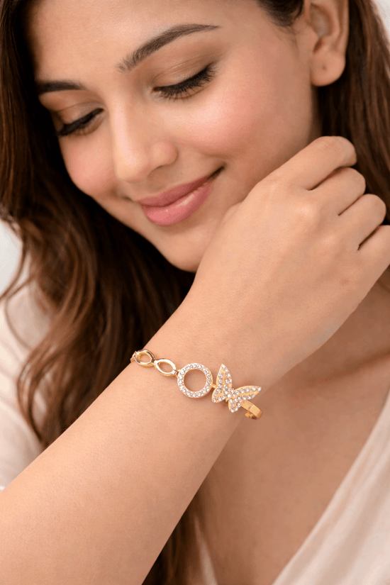 Woman wearing a gold bracelet with butterfly charm on a plain background