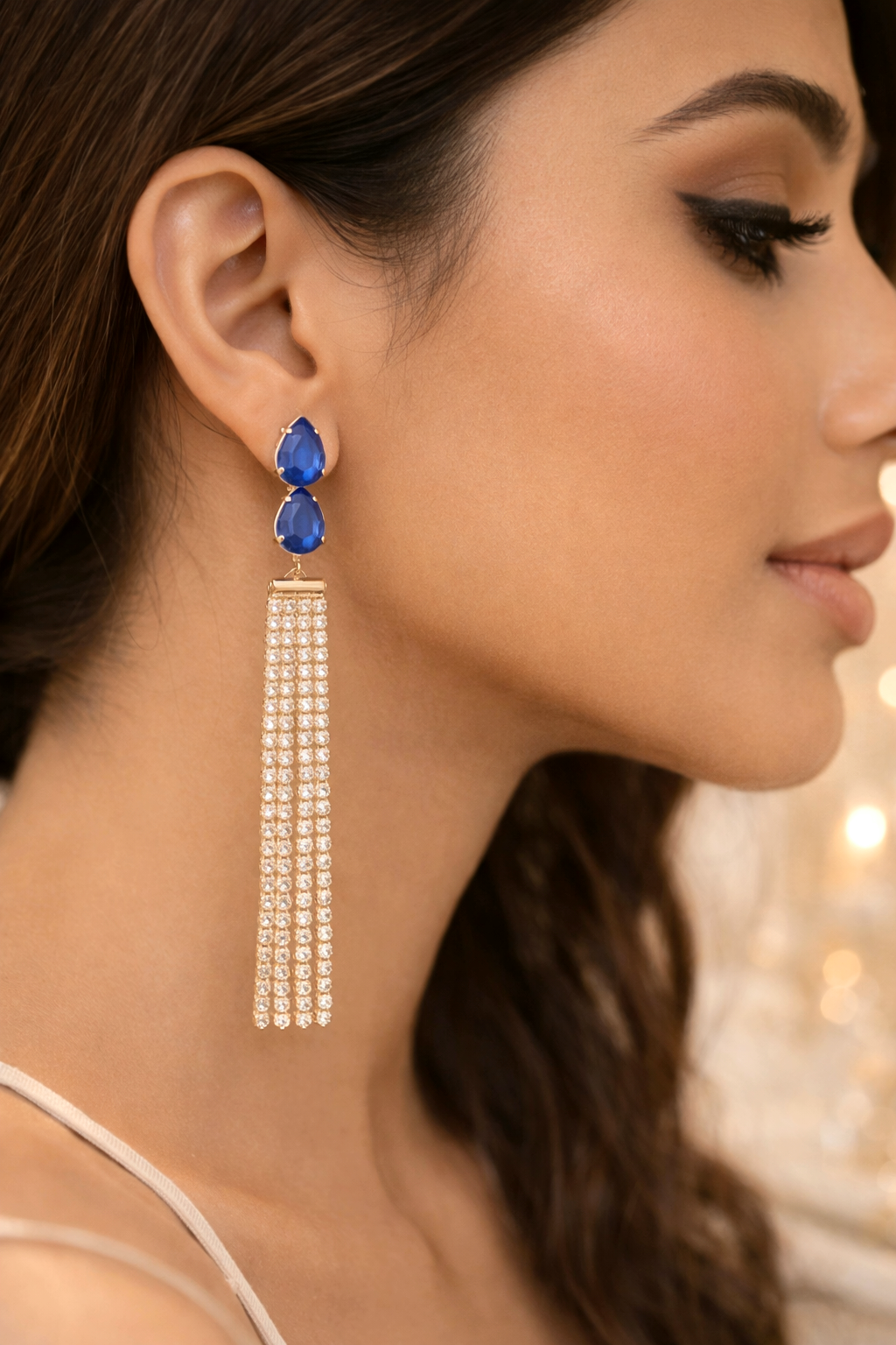 Close-up of a woman wearing a long, dangling earring with blue gemstones.