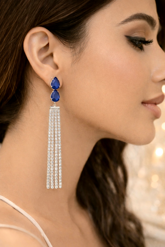 Close-up of a woman wearing a pair of earrings with blue gemstones and silver tassels.