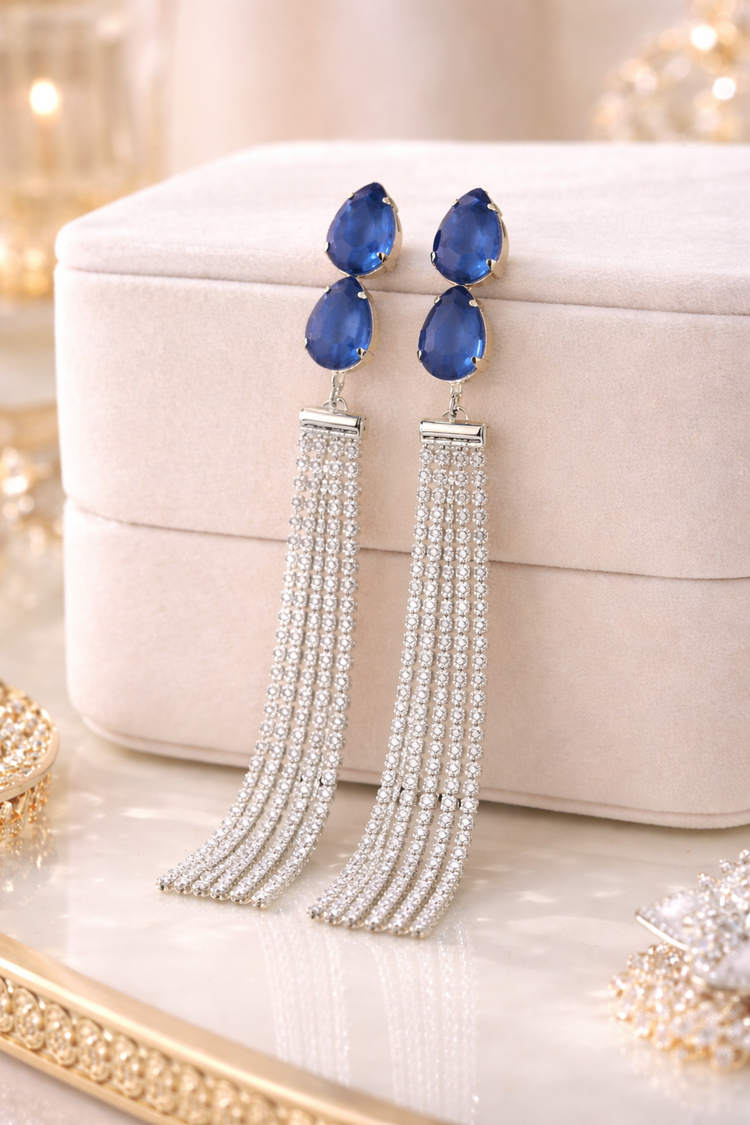 Pair of blue teardrop earrings with silver tassels on a decorative surface.